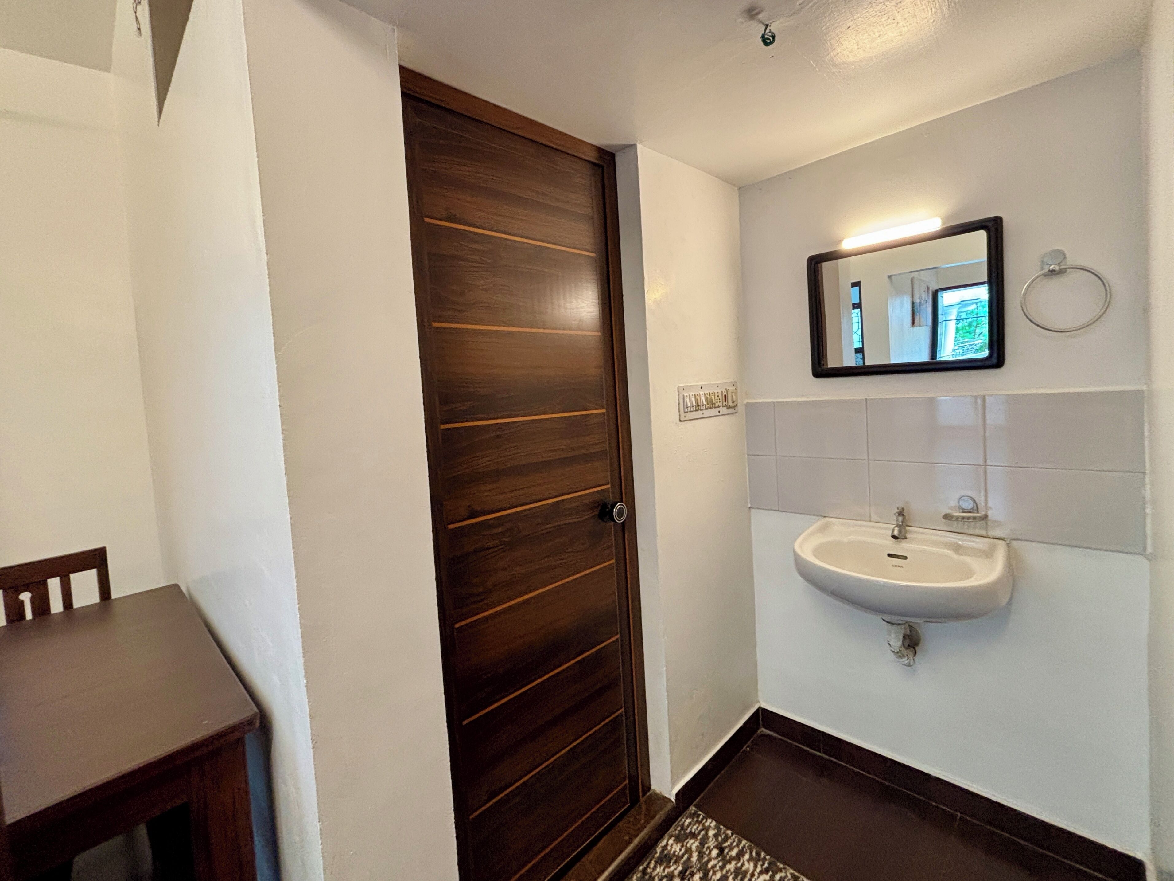 Un baño con puerta de madera, un lavamanos blanco y un espejo encima.