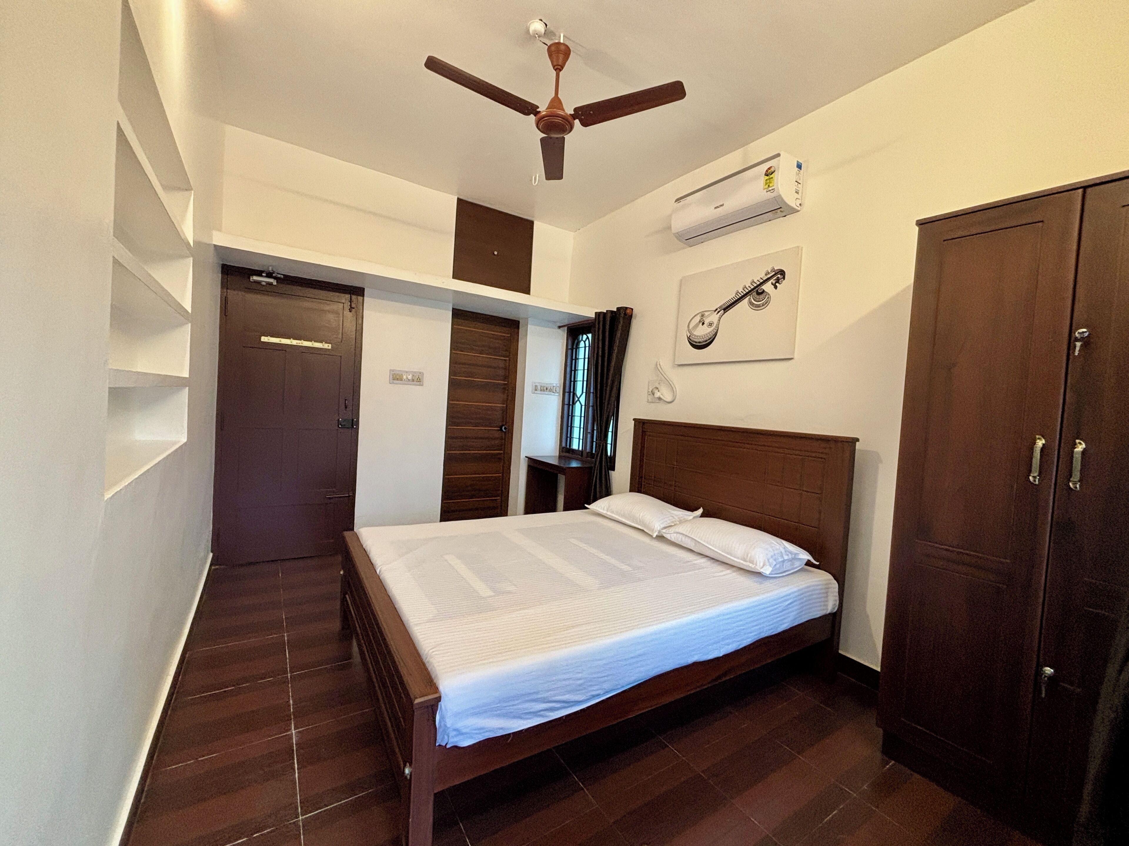 A bedroom with a wooden bed, a ceiling fan, an air conditioning unit, and a wardrobe.