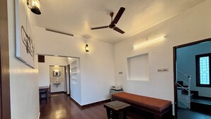 A spacious room with a wooden floor, a ceiling fan, a bed, a small table, and a staircase leading to another level. - Fort Grande Stay  (Kochi)