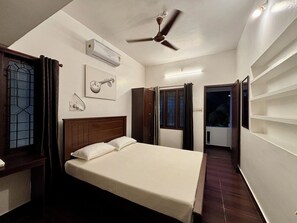 A bedroom with a bed, an air conditioning unit, a ceiling fan, a window with curtains, and a door leading to a balcony. - Fort Grande Stay  (Kochi)