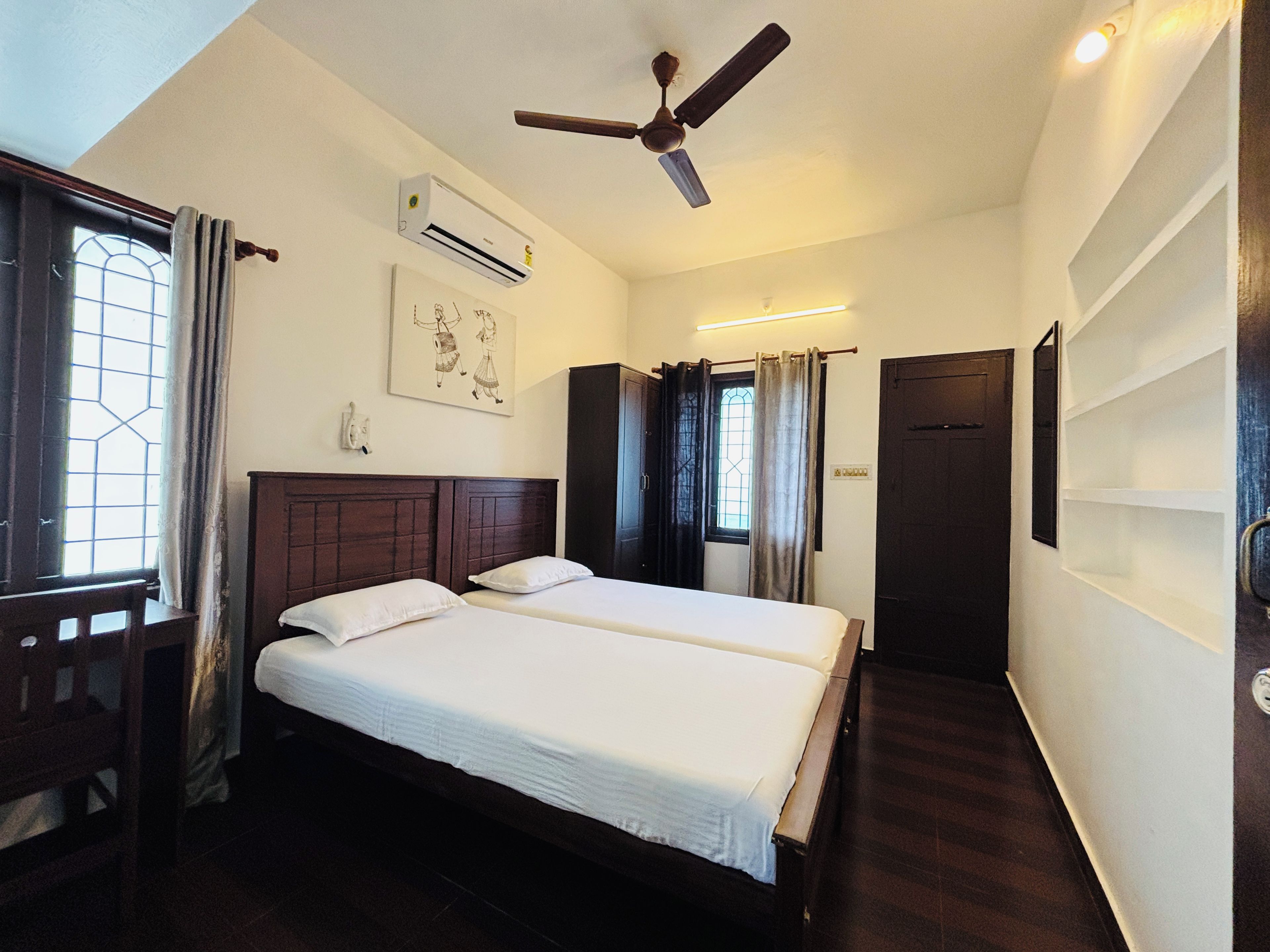 A hotel room with two beds, a ceiling fan, an air conditioning unit, a window with curtains, and a door.