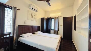 A hotel room with two beds, a ceiling fan, an air conditioning unit, a window with curtains, and a door.