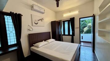 Un dormitorio con cama, aire acondicionado, ventilador de techo, ventana con cortinas, una lámpara de pared y una puerta que da a un balcón.
