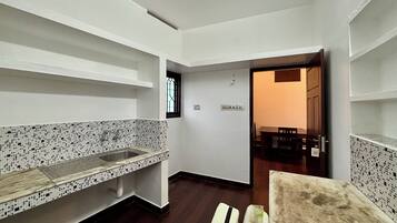 Cozinha com painel de azulejos, pia e janela. É possível ver uma área de jantar com mesa e cadeiras através de uma porta aberta.