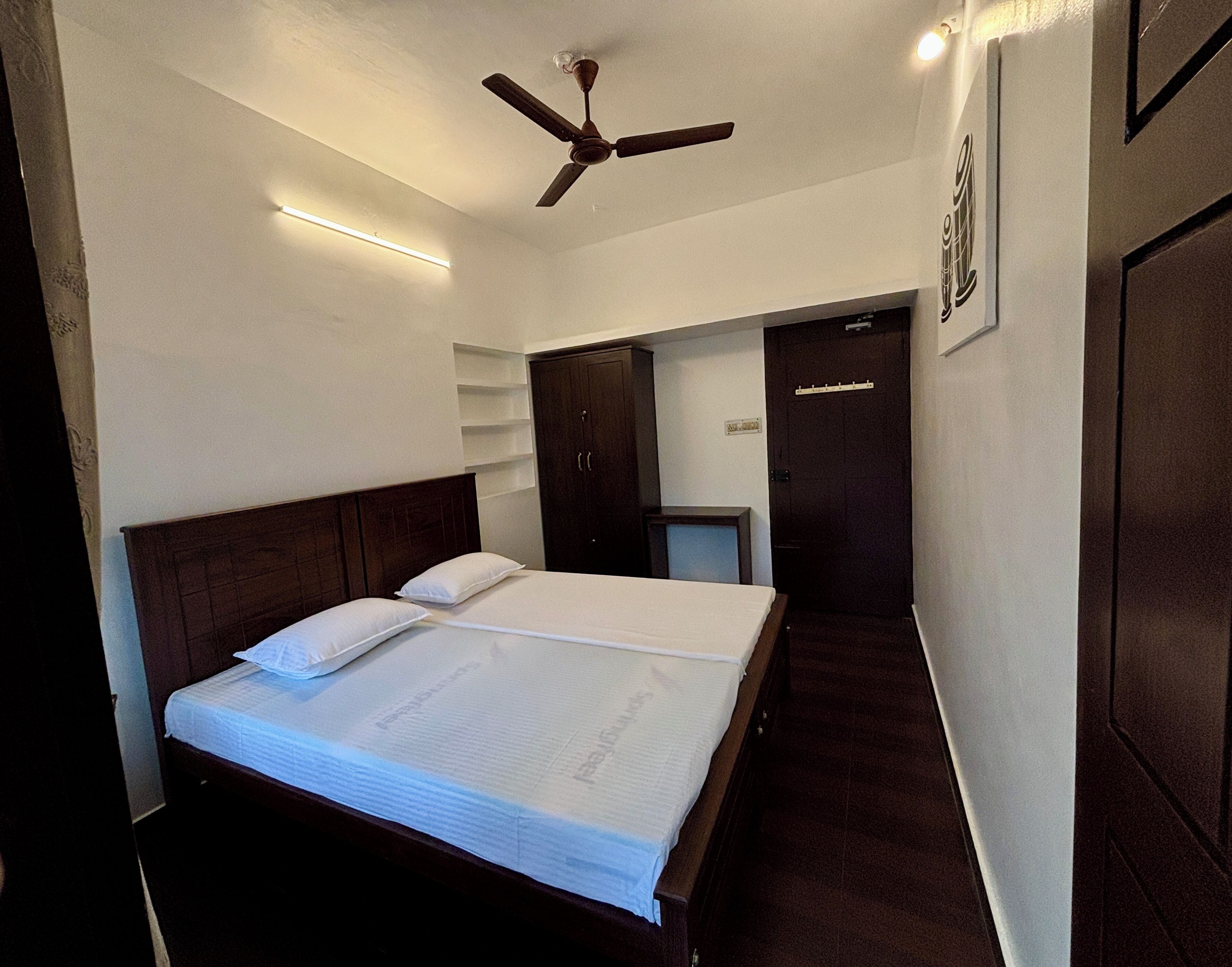 A hotel room with a large bed, a ceiling fan, a wardrobe, and a desk with a chair.