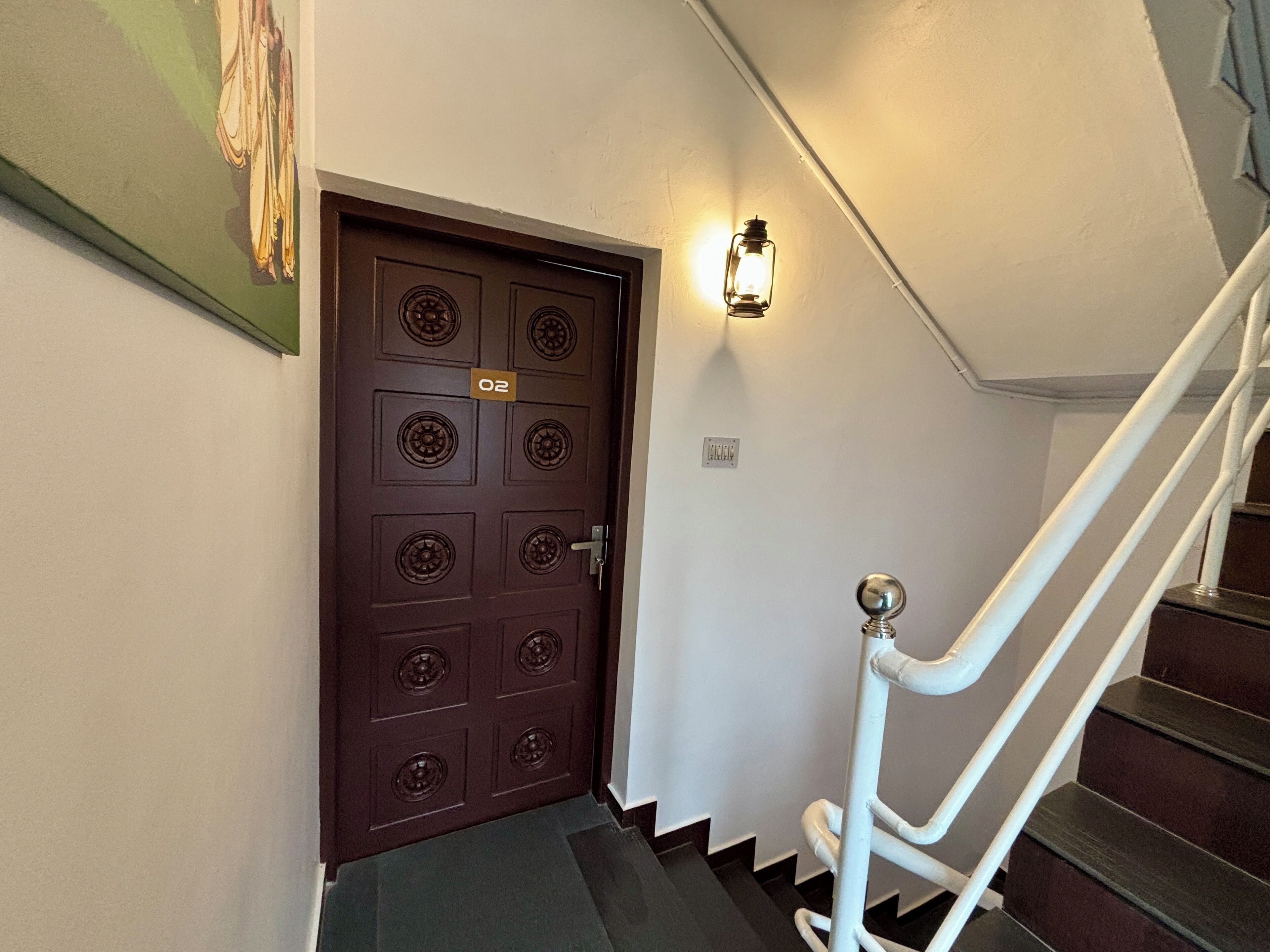 A brown door with a number plate, a white wall, and a white staircase.
