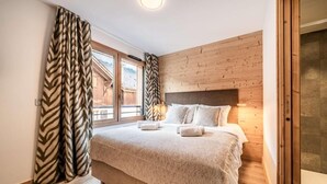 A bedroom with a large bed, wooden walls, and a view of a wooden building outside. - 100m from resort center, 2nd floor, view village, terrace, tv, 84m², Morzine (Morzine)