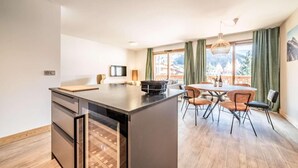 A modern kitchen with a central island, dining area with chairs, and large windows with curtains. - 100m from resort center, 2nd floor, view village, terrace, tv, 84m², Morzine (Morzine)
