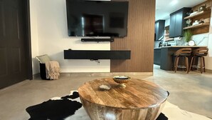 Een moderne woonkamer met een ronde houten salontafel, een wandgemonteerde televisie en een zwart-wit koeienhuidtapijt.