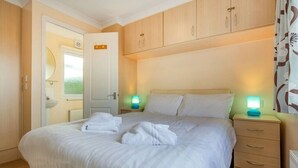 Uma cama bem arrumada com lençóis e toalhas brancos, um guarda-roupa de madeira e abajures.