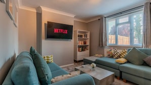 A living room with a sofa, a coffee table, a bookshelf, and a TV mounted on the wall.