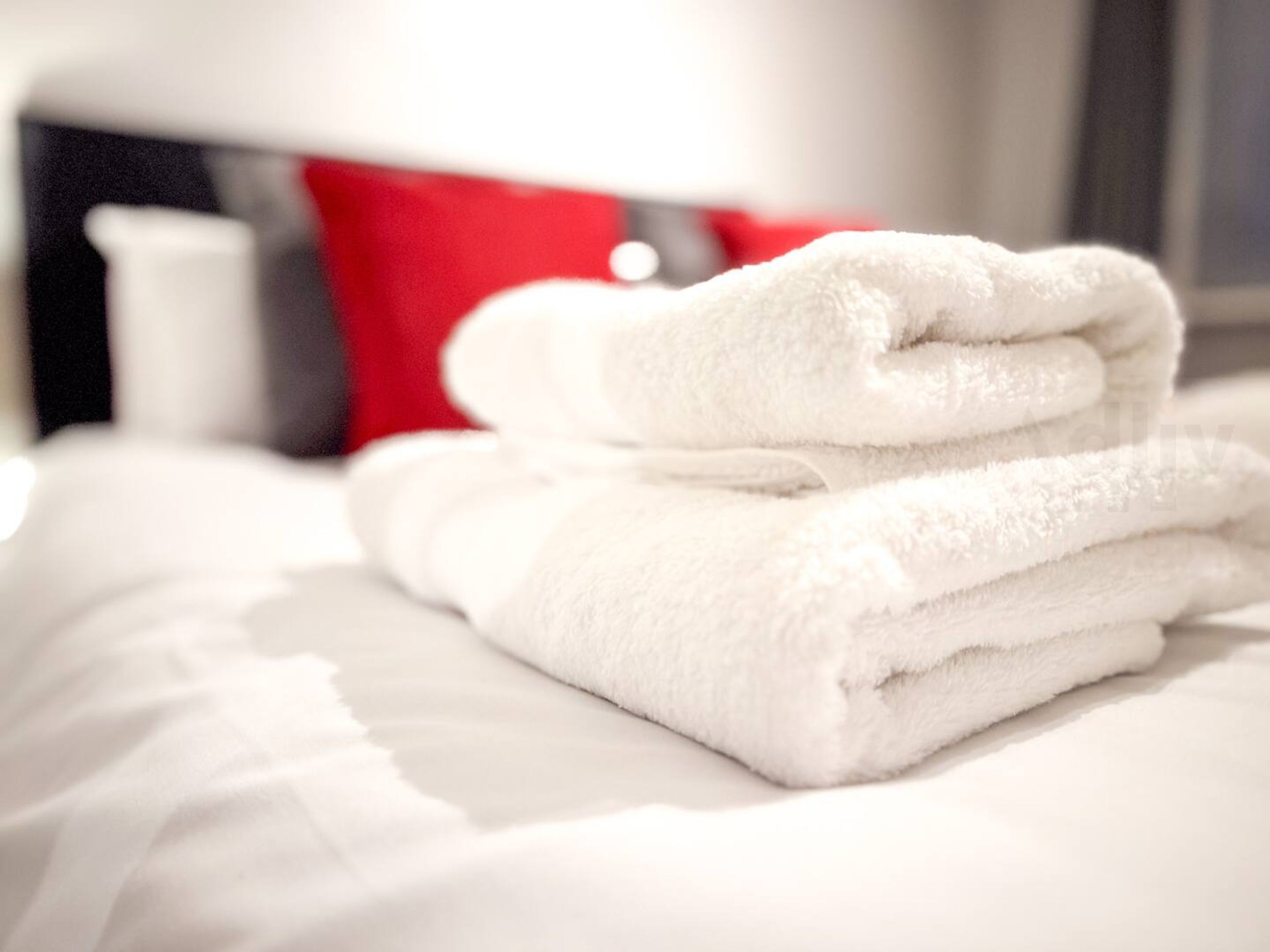 A neatly made bed with white linens and a stack of white towels.
