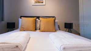 A neatly made bed with two white towels, a headboard, and two bedside lamps.