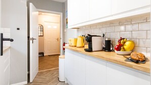 A kitchen with white cabinets, a wooden countertop, and various kitchen items like a coffee maker, a bowl of fruit, and a loaf of bread.