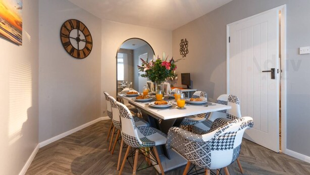 A dining area with a white table, patterned chairs, and a large wall clock.