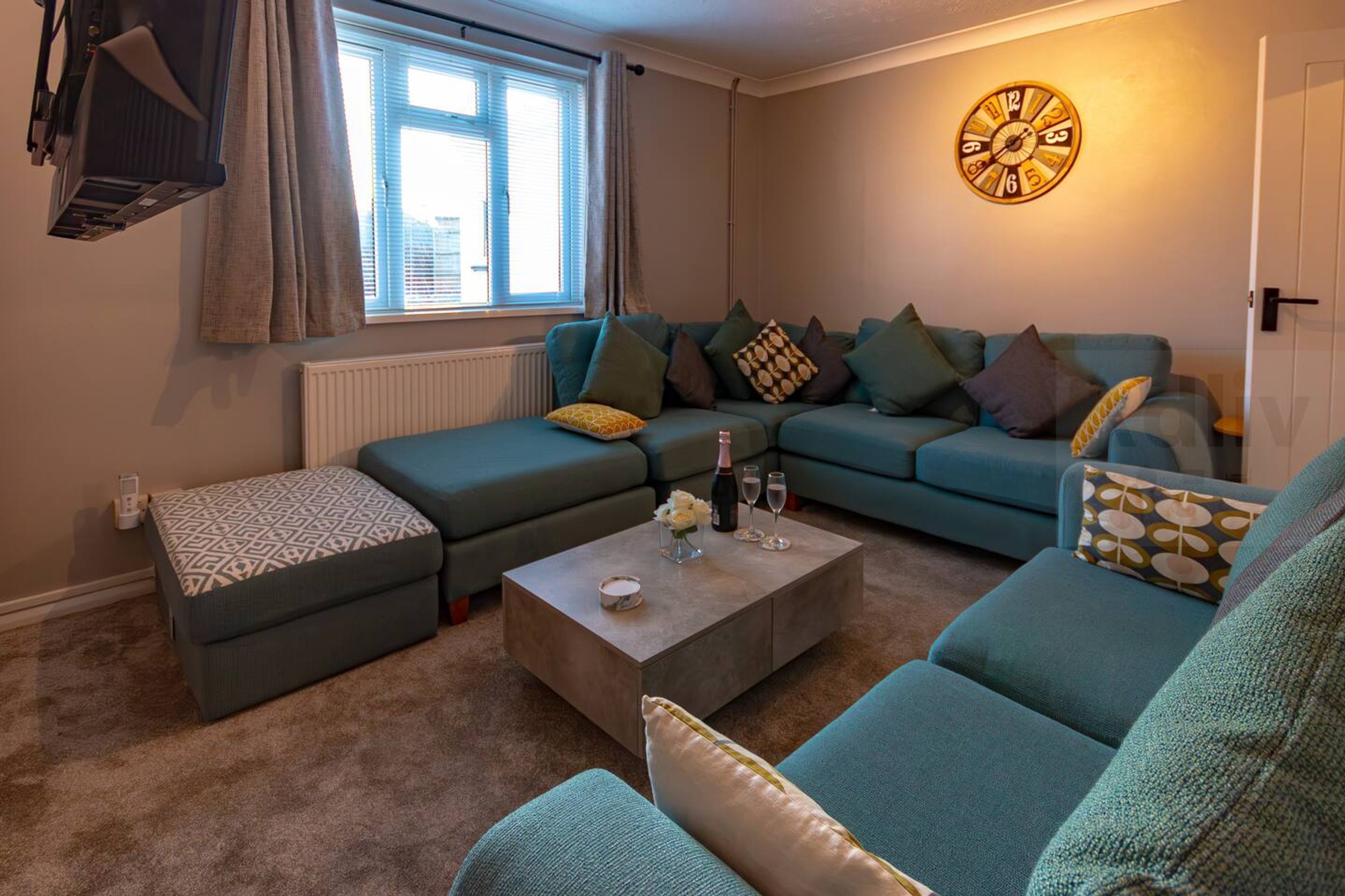 A living room with a sectional sofa, a coffee table, and a wall clock.