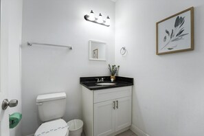 A bathroom with a white toilet, a black sink, and a white cabinet. There is a mirror above the sink and a framed picture on the wall.