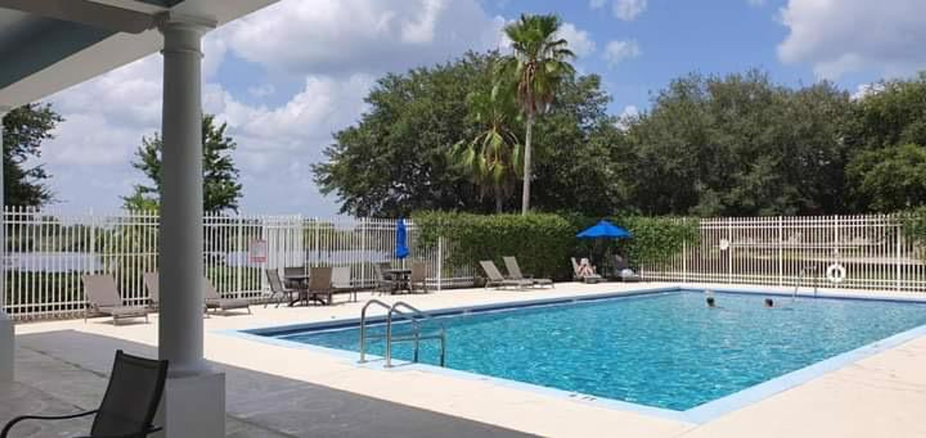 A rectangular swimming pool with a metal ladder, surrounded by a white fence.