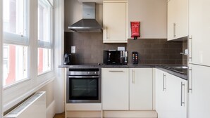 A modern kitchen with white cabinets, a stainless steel range hood, a built-in oven, a microwave, and a coffee maker.