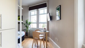 A modern kitchen with wooden cabinets, a dining table with chairs, a potted plant, and a window with blinds.