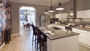 Een moderne keuken met een centraal eiland, roestvrijstalen apparatuur en hangende lampen.