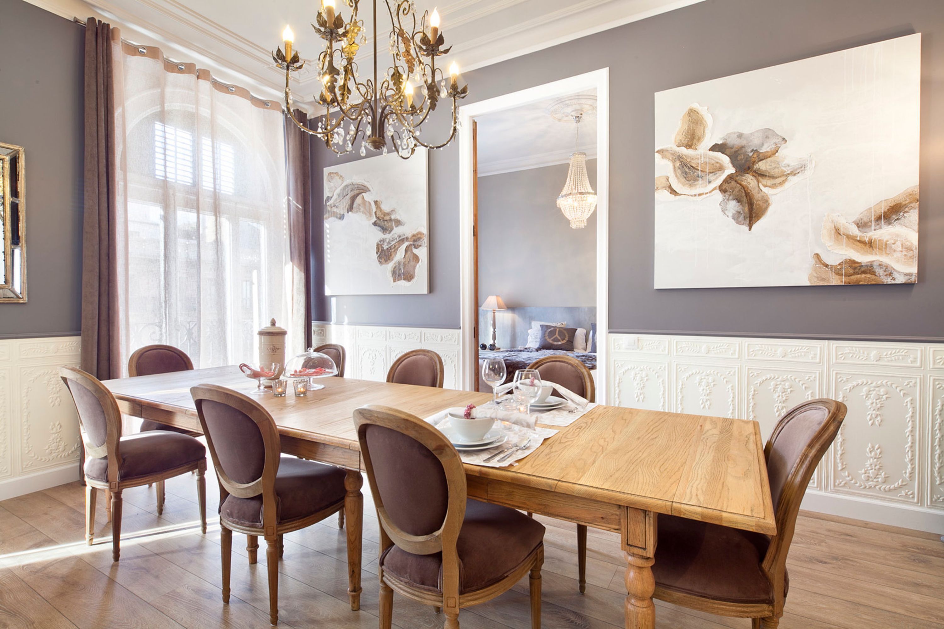 Une salle à manger avec une table en bois dressée pour six personnes, entourée de chaises rembourrées.