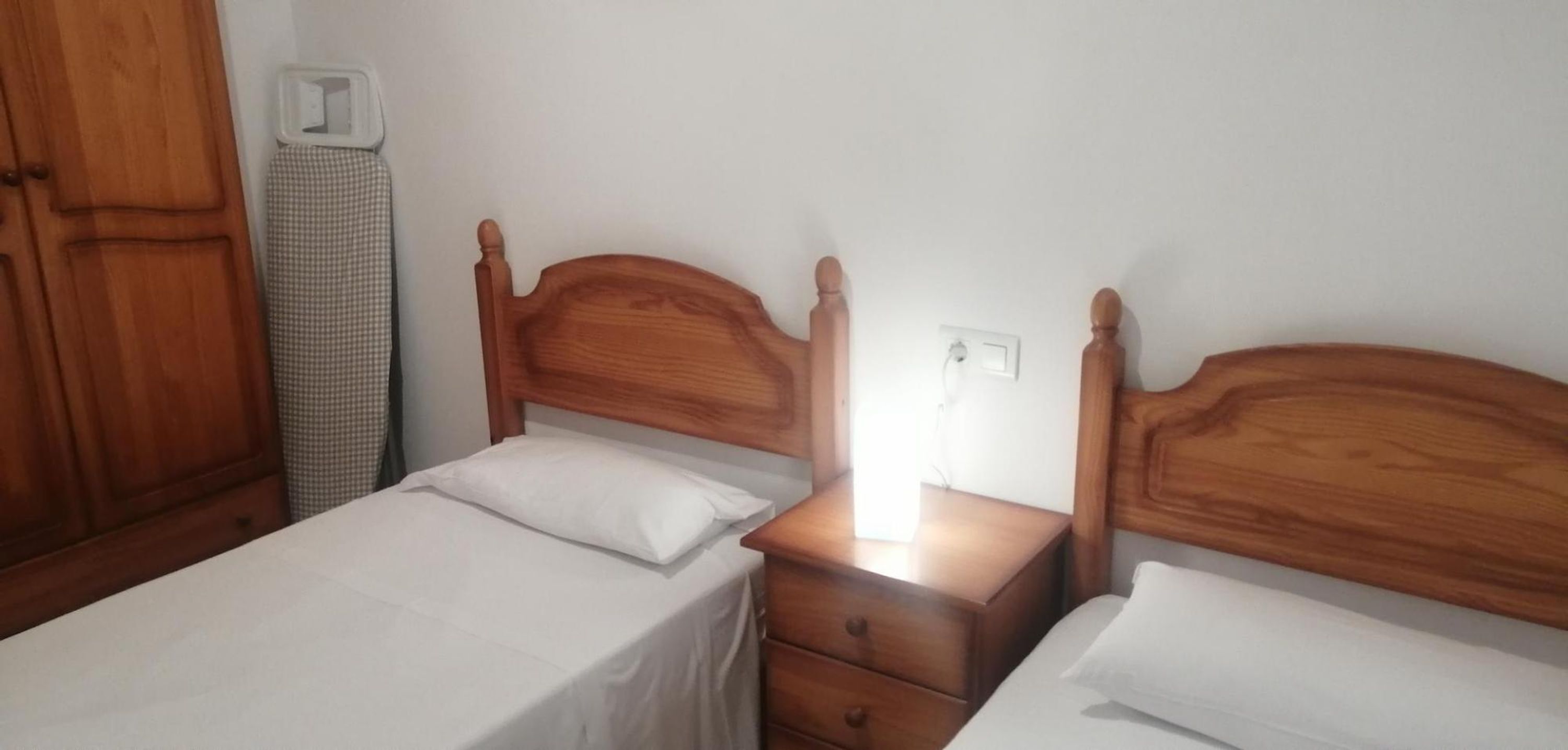 A bedroom with two wooden beds, a nightstand, and a wardrobe.