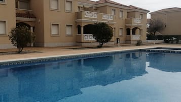 Una piscina amb una superfície d'aigua blava i transparent, envoltada per un edifici beix amb balcons i finestres.