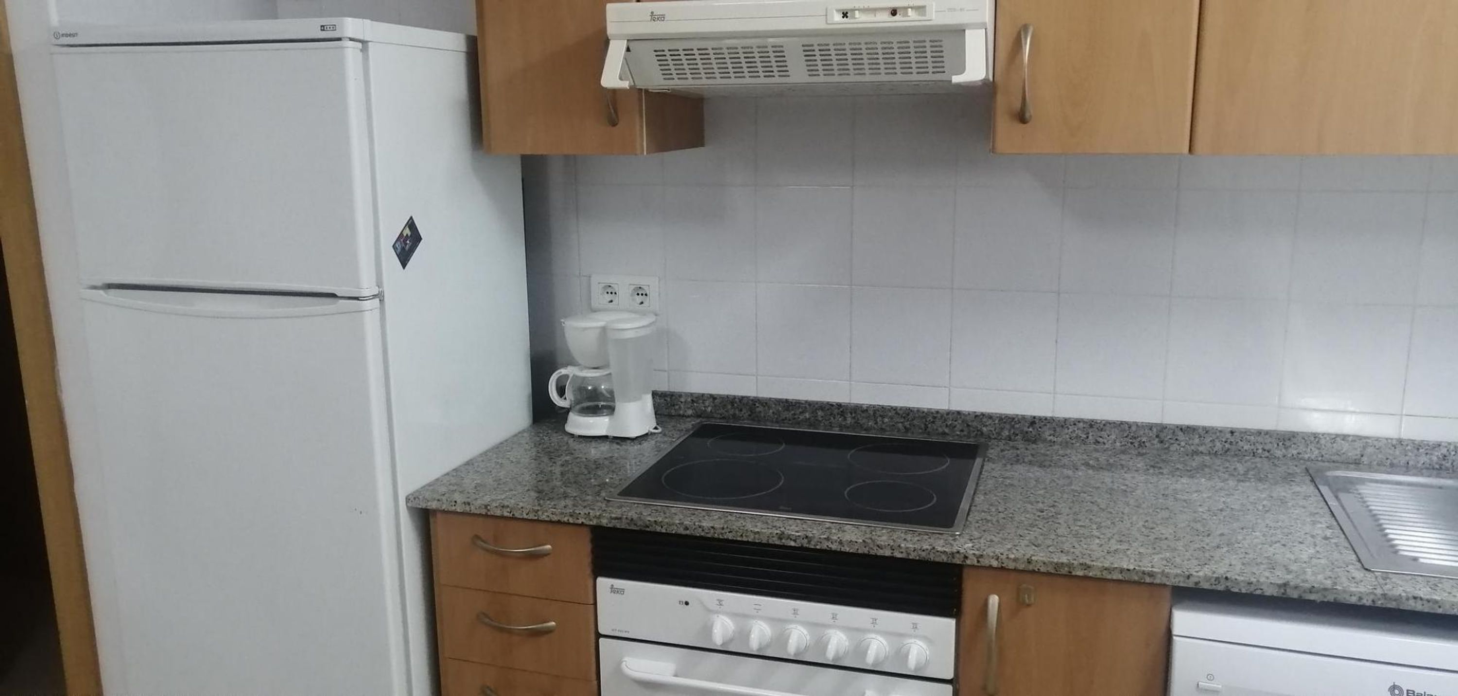 Una cocina compacta con un refrigerador blanco, cafetera, estufa y lavavajillas.
