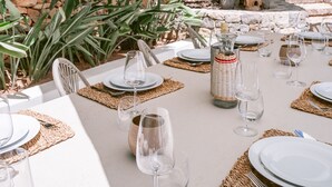 An outdoor dining area with tables set for a meal, surrounded by lush tropical plants and a stone wall. - Can Furnet in Ibiza With 4 Bedrooms and 8 Bathrooms (Santa Eulalia del Rio)