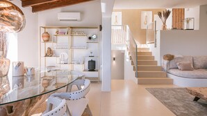 A modern living room with a glass dining table, white sofas, a staircase, and a bookshelf with decorative items. - Can Furnet in Ibiza With 4 Bedrooms and 8 Bathrooms (Santa Eulalia del Rio)