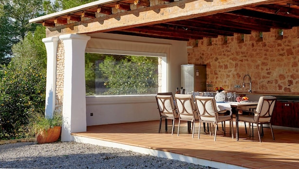 An outdoor patio with stone walls, a pergola, and a dining area with chairs and a table.