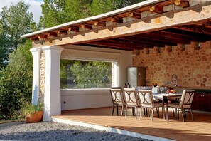 An outdoor patio with stone walls, a pergola, and a dining area with chairs and a table. - Villa Munt Blanc Ibiza (Sant Antoni de Portmany)