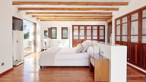 A spacious bedroom with a large bed, wooden beams on the ceiling, and a view of the outdoors.