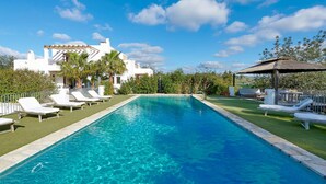 A rectangular swimming pool with clear blue water, surrounded by white lounge chairs and a well-maintained lawn.