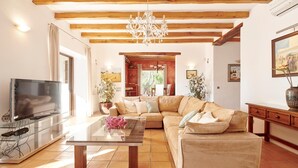 A living room with a sofa, a glass coffee table, a TV, and wooden beams on the ceiling.