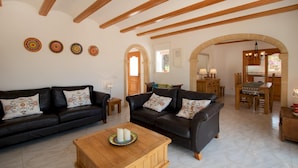 A spacious living area with two black leather sofas, a wooden coffee table, and a dining table with chairs. There are wooden beams on the ceiling and a chandelier. - Villa Margarite in Javea (Javea)