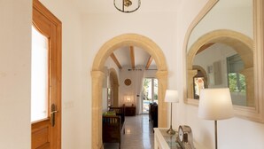 A hallway with arched doorways, a bench, a lamp, and a clock on a console table. - Villa Margarite in Javea (Javea)