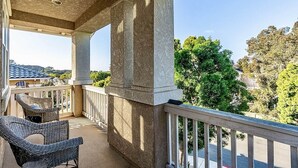A balcony with wicker chairs, a stone balustrade, and a view of trees and buildings.