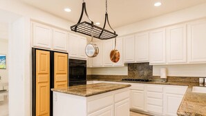 A kitchen with white cabinets, a granite countertop, a black refrigerator, and a hanging pot rack.
