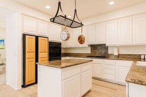 Una cocina con gabinetes blancos, encimera de granito, refrigerador negro y una estantería para ollas colgante.