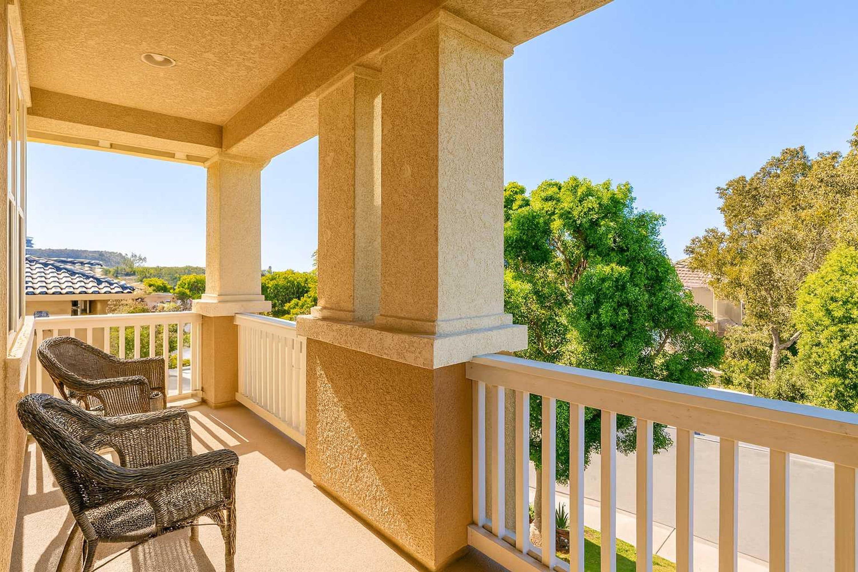 A balcony with wicker chairs, white railings, and a view of trees and buildings.