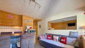 Una habitación acogedora con una mesa de comedor de madera, un sofá con almohadones con motivos de esquí, y una zona de cocina con armarios de madera y un microondas.