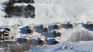 Un grupo de cabañas de madera con tejados nevados, ubicadas frente a una ladera cubierta de nieve.
