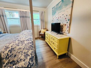 A bedroom with a four-poster bed, a yellow dresser, a television, and a large painting on the wall.