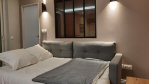 A neatly made bed with white and gray linens, a gray throw blanket, and a headboard with a mirror. There are two wall-mounted lights on either side of the mirror. - The magnolia (Hautot-sur-Mer)