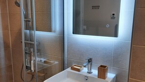 A modern bathroom with a glass-enclosed shower, a white sink with a wooden cabinet, and a mirror above the sink. - The magnolia (Hautot-sur-Mer)