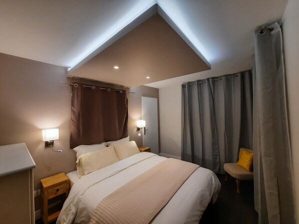 Una habitación de hotel con cama, lámparas de noche, mesita de noche, una silla y ventana con cortinas.