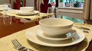 A dining table set with white plates, bowls, and cutlery, with a view of greenery outside through a window. - *Port Clinton*3 BedRM*SunRM*Fenced Yard*Near Beach/Park/Lighthouse/Restaurants* (Port Clinton)