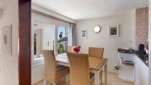 Ein Essbereich mit Korbstühlen, einem Holztisch und Blick durch ein großes Fenster.